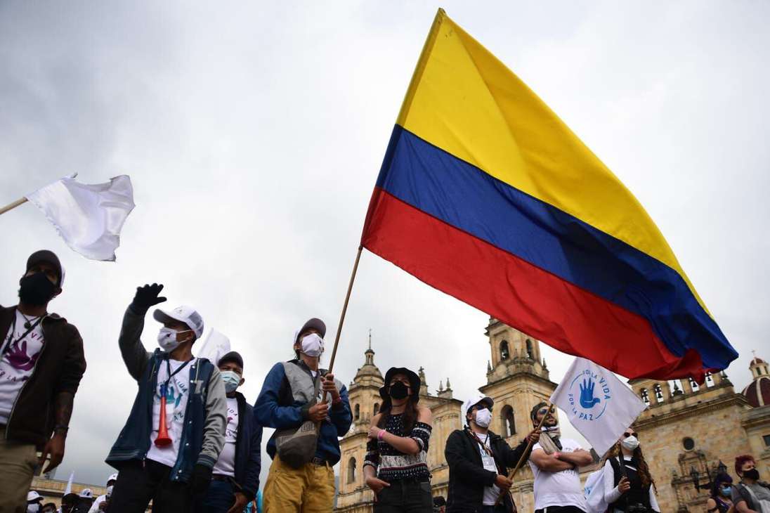 un grupo de personas se en encuentras reunidas con bandera de colombia y objetos identitarios al partido Farc y a la paz.