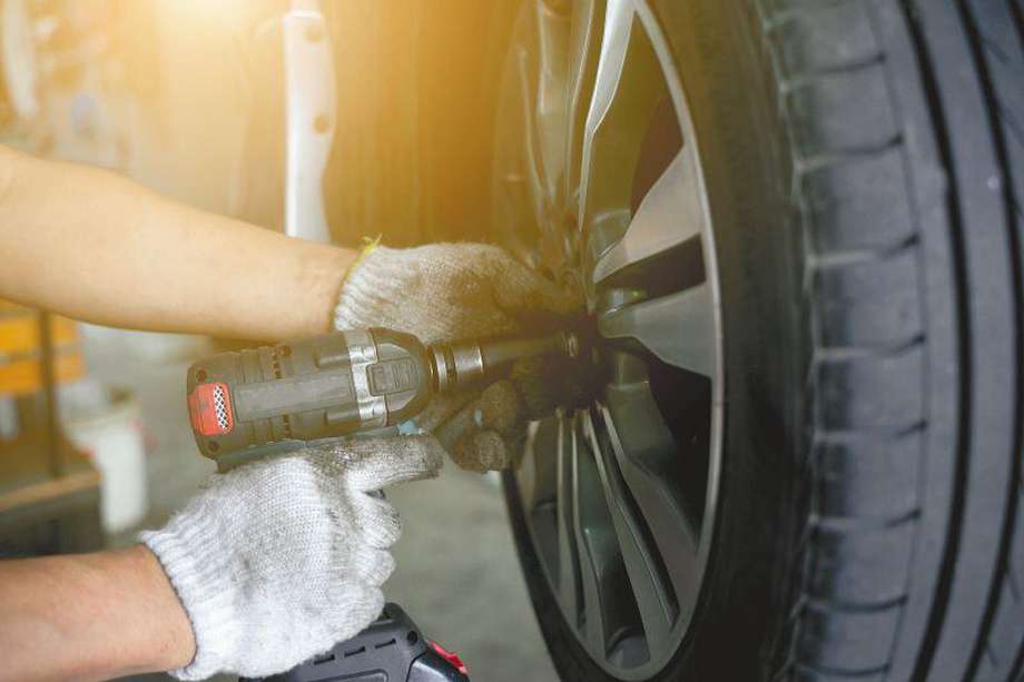 Detail image of mechanic hands with tool, changing tyre of car, with blurred background of garage.