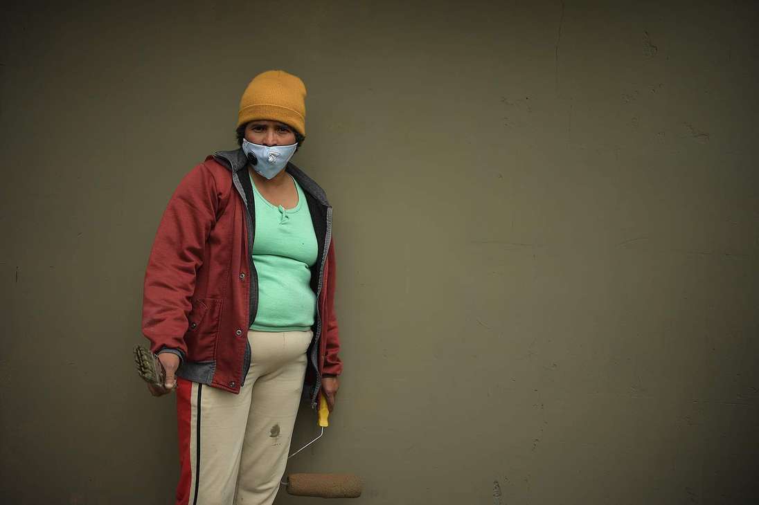 Mujer sosteniendo un rodillo en una pared gris.