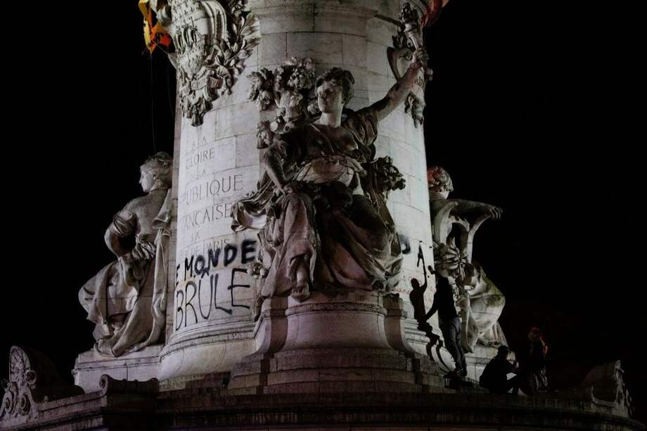 Manifestantes cuelgan un cartel que dice "El mundo arde" en la estatua de la Place de la Republique en París.