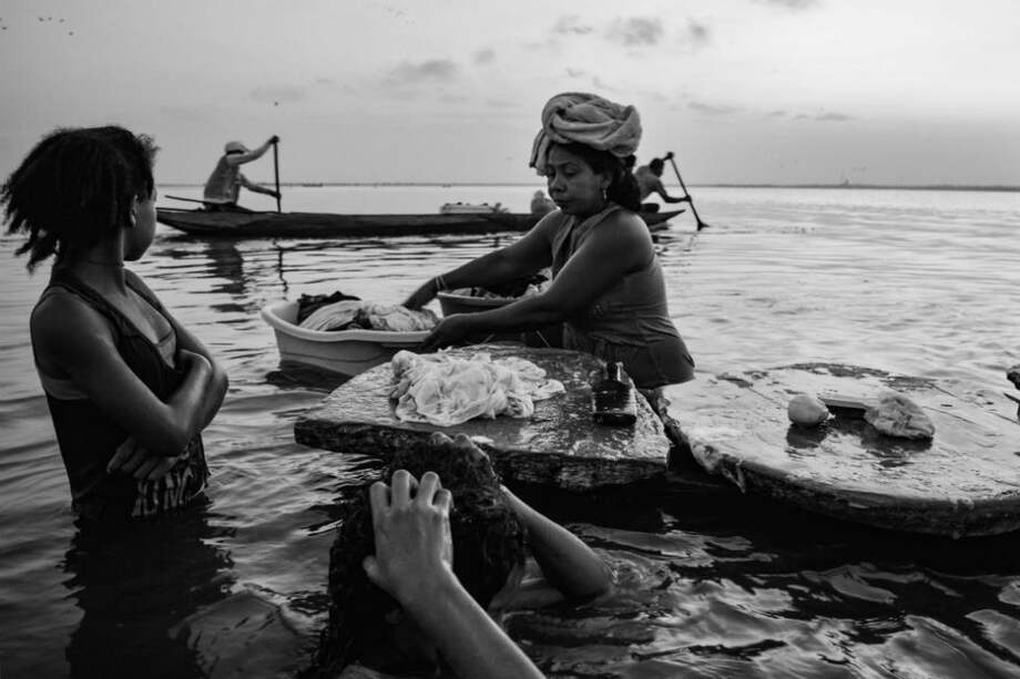 Una niña lava su cabello mientras la lavandera acomoda la ropa en su ponchera y los hombres se van a pescar.