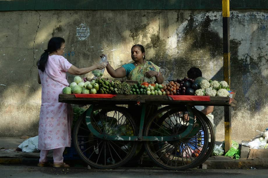 Una mujer india vende verduras a un cliente en su tienda ambulante en Mumbai. / AFP