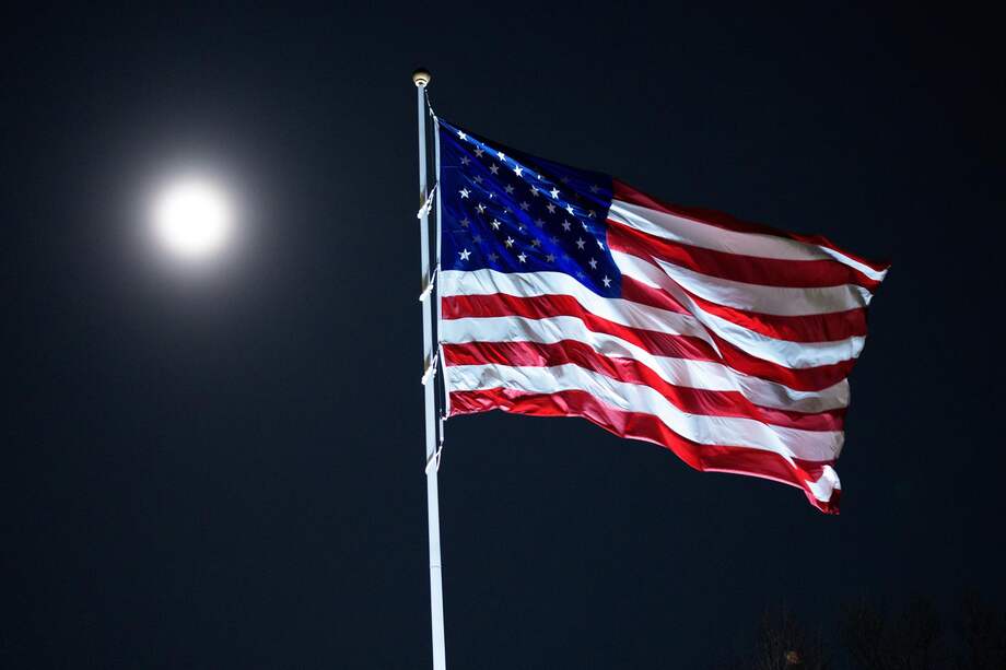 La luna sale mientras la bandera estadounidense ondea en la Casa Blanca en Washington.
