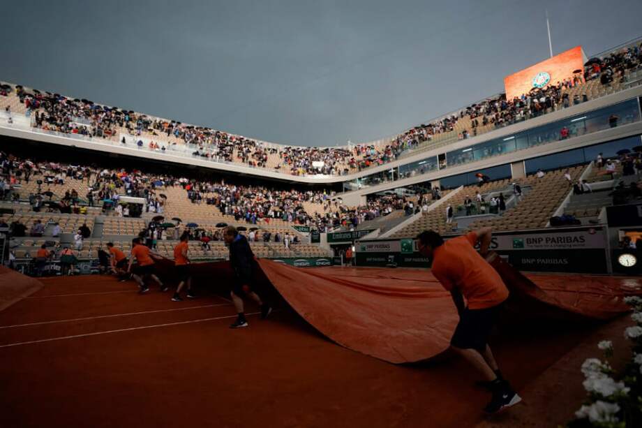 Los miembros del personal de campo colocan coberturas en la superficie de la cancha cuando cae la lluvia durante el partido entre el español Rafael Nadal y el japonés Kei Nishikori. / AFP