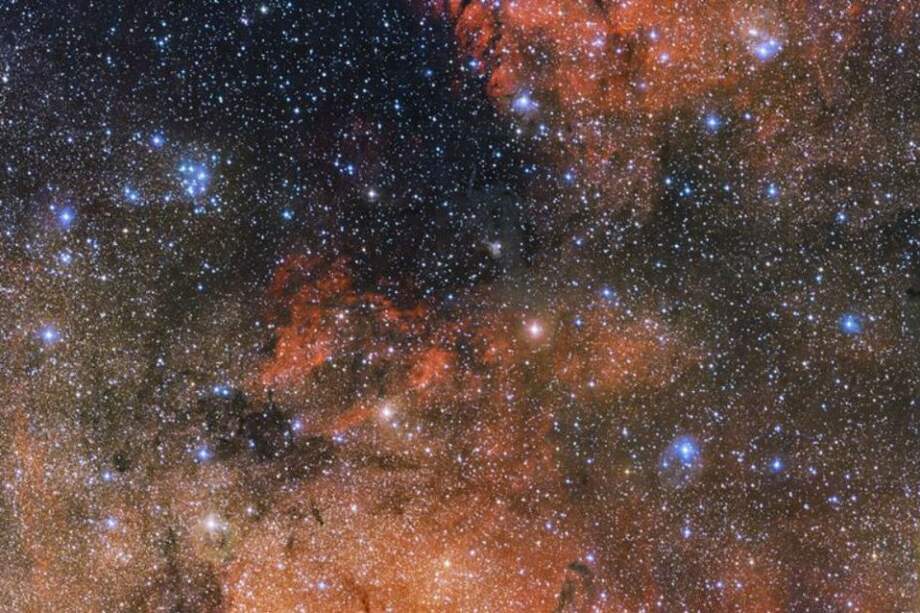 La imagen muestra un puñado de llamativas estrellas azules y nubes rojas de hidrógeno ionizado brillante y oscuros filamentos de polvo. Los trazos oscuros que serpentean a través de la imagen son los turbios hilos de polvo cósmico que bloquean la luz de las estrellas distantes. / EFE