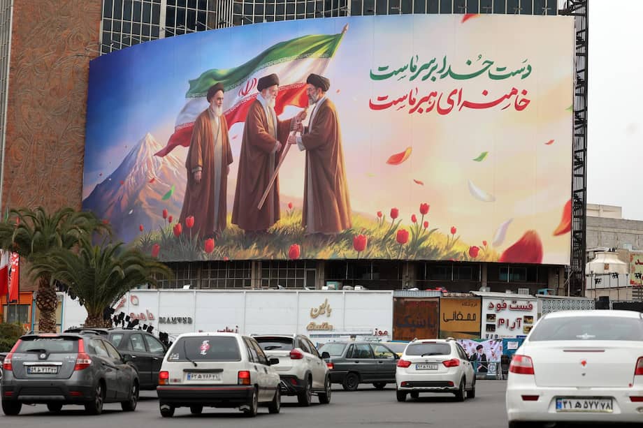La gente pasa frente a un enorme cartel que muestra a los difuntos líderes supremos iraníes, el ayatolá Ruhollah Jomeini (izq.), el ayatolá Ali Jamenei (centro) y el nuevo líder supremo iraní, el ayatolá Mojtaba Jamenei (der.).