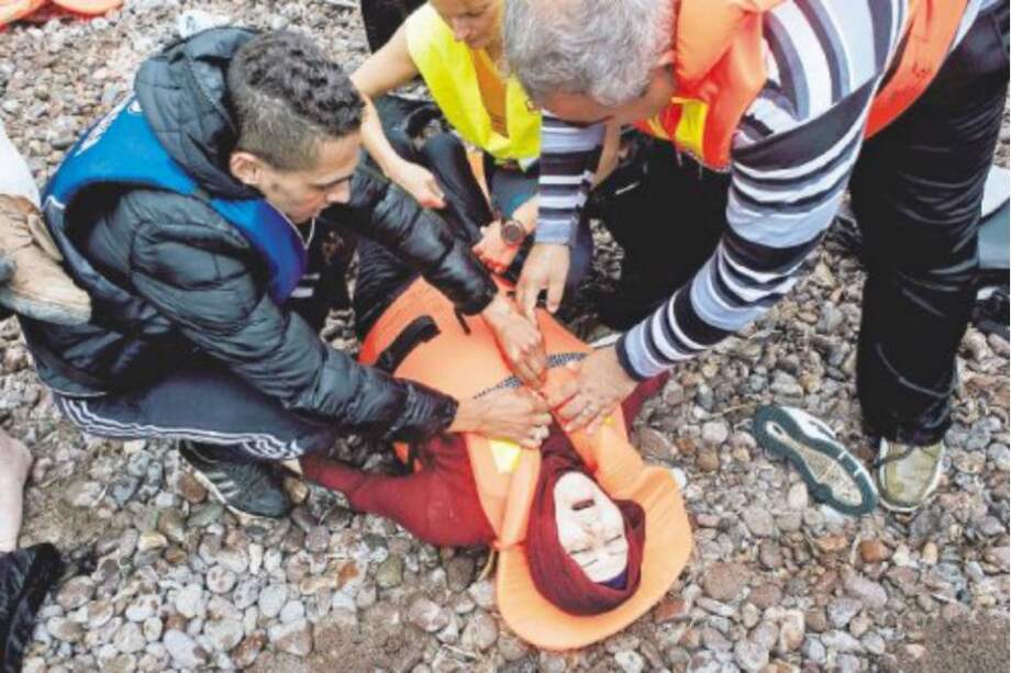 Migrantes auxilian a una mujer en la isla de Lesbos después de su tránsito por Turquía. / AFP