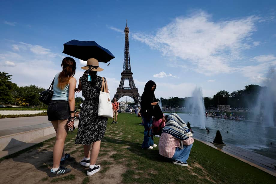 Varias mujeres se resguardan del calor bajo una sombrilla en la fuente del Trocadero, junto a la Torre Eiffel, en París.
