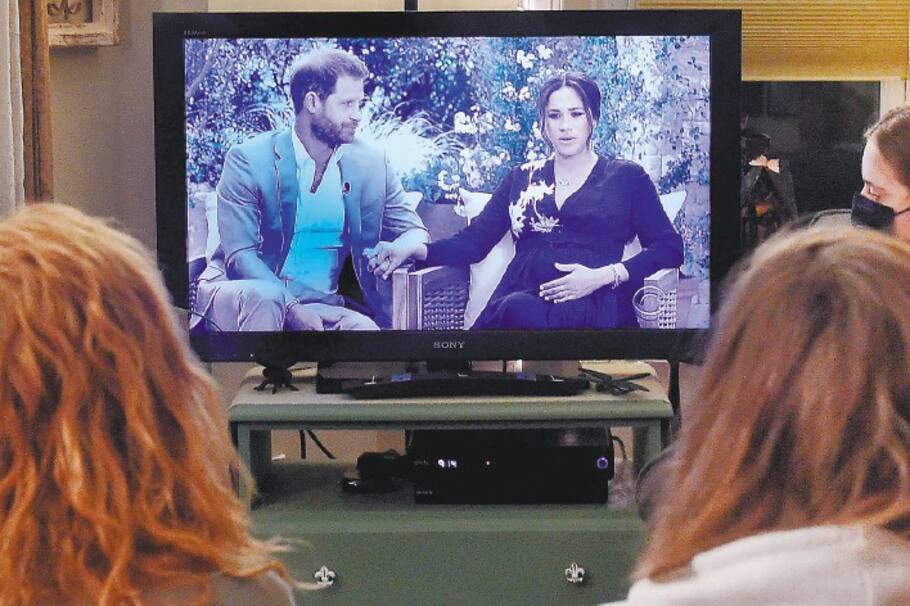 TOPSHOT - This photo illustration shows people wearing face masks, watch a televised conversation between Britain's Prince Harry with his wife Meghan Markle and US host Oprah Winfrey, in Arlington, Virginia March 7, 2021. Britain's royal family on Sunday braced for further revelations from Prince Harry and his American wife, Meghan, as a week of transatlantic claim and counter-claim reaches a climax with the broadcast of their interview with Oprah Winfrey. The two-hour interview with the US TV queen is the biggest royal tell-all since Harry's mother princess Diana detailed her crumbling marriage to his father Prince Charles in 1995. / AFP / OLIVIER DOULIERY