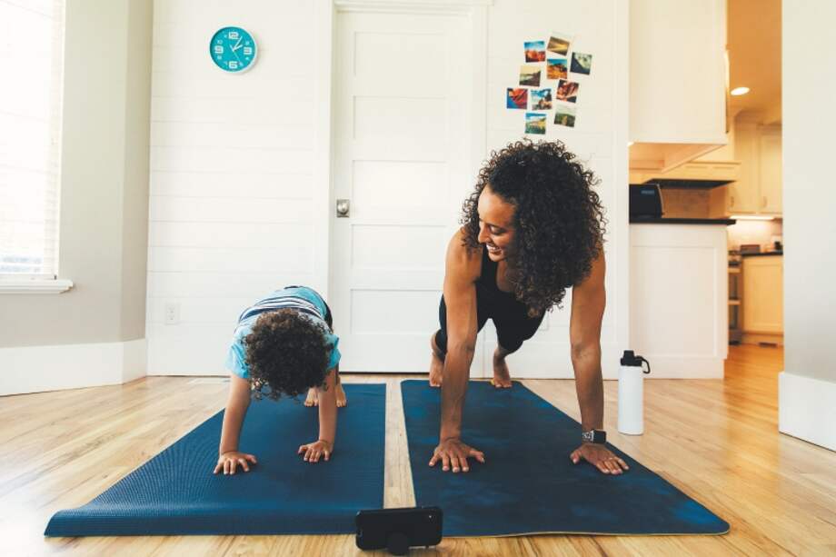 A mother exercises with her young son inside their home. She is teaching the boy the importance of a healthy lifestyle by proper stretching and exercising.