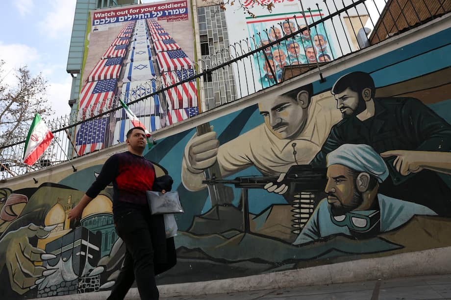 Un hombre iraní camina junto a una pintura mural de soldados iraníes (abajo) cerca de una valla publicitaria anti-EE. UU. e Israel (arriba) en Teherán, Irán.