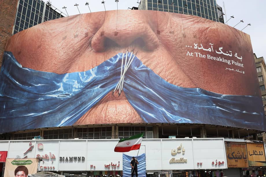 Un hombre ondea la bandera de Irán delante de una propaganda antiestadounidense en Teherán.