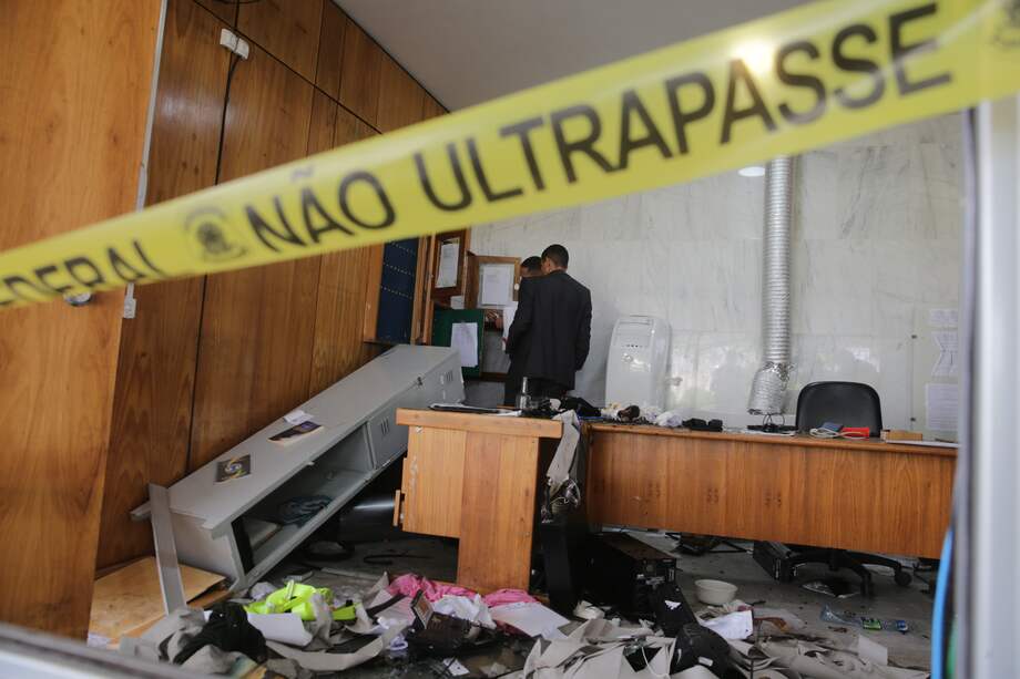 Dos hombres revisan una oficina destrozada al interior del Palacio de Planalto, luego de que unos manifestantes bolsonaristas se tomaran la Plaza de los Tres Poderes para invadir los edificios gubernamentales.