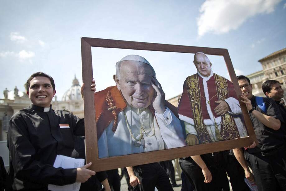 Dos jóvenes sacerdotes pertenecientes a los Legionarios de Cristo sostienen una imagen del papa Juan Pablo II y Juan XXIII junto a la basílica de San Pedro en el Vaticano. /EFE