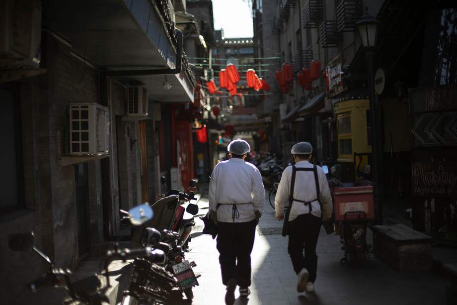 Dos trabajadores de un restaurante caminan por una calle de Beijing, China.