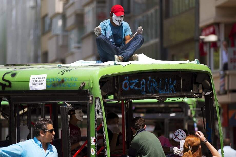 Un manifestante con una máscara de Anonymus reza encima de un autobús cerca del parque Gezi en la plaza Taksim en Estambul (Turquía)./ efe