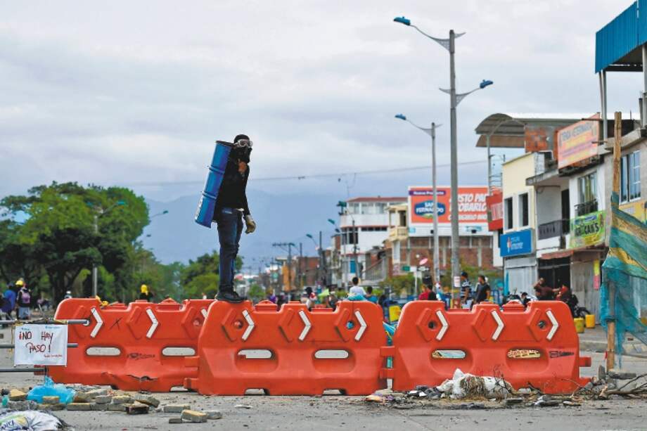 A demonstrator stands guard in a street blocked with a barricade during a protest against the government of Colombian President Ivan Duque, in Cali, Colombia, on May 22, 2021. / AFP / Luis ROBAYO