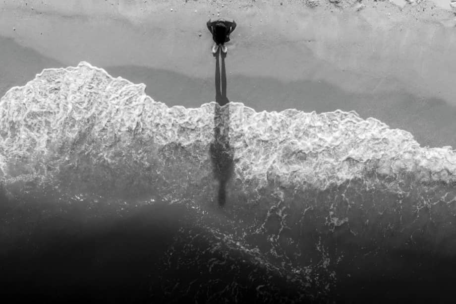 A man who stands alone in the midst of the waves that enter the sand.