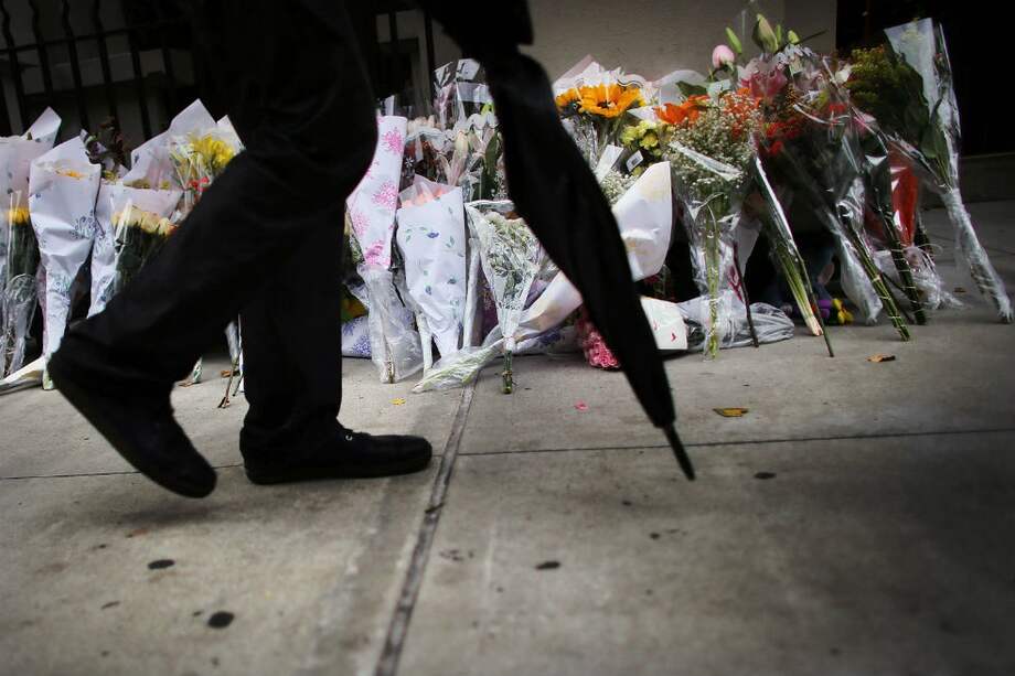 un hombre con una sombrilla camina junto a flores que han quedado frente al edificio donde los dos niños fueron apuñalados por su niñera en el apartamento de una familia del Upper West Side en la ciudad de Nueva York. / AFP