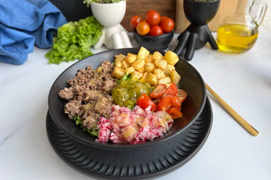 Los ingredientes infaltables para este tazón de hamburguesa son el tomate, la cebolla, la papa y los pepinillos.