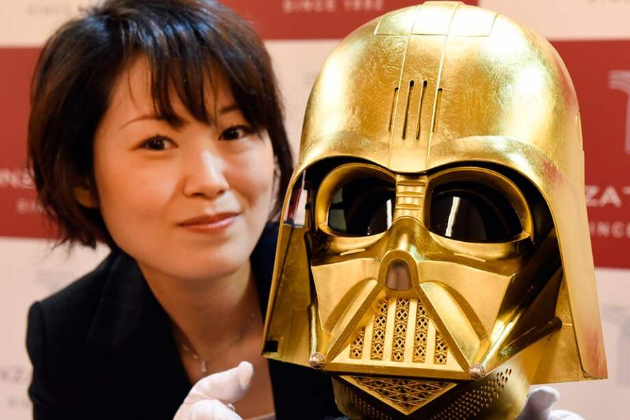 empleada de la joyería Tanaka Kikinzoku posa junto a una máscara de Darth Vader bañada en oro en la tienda Ginza Tanaka en Tokio (Japón). / AFP