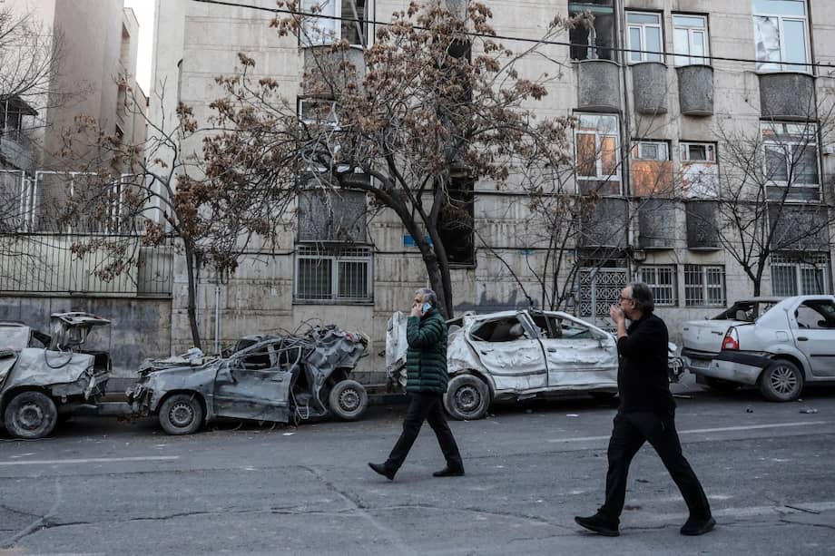 Dos hombres caminan entre los restos de carros y junto a edificios residenciales dañados cerca de la plaza Niloufar de Teherán.