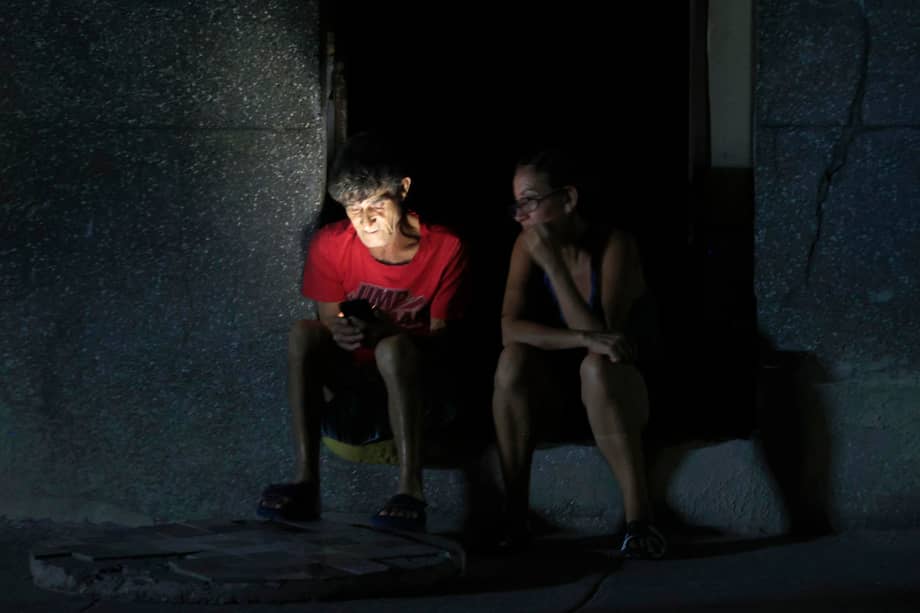 Personas observan un teléfono durante un apagón este jueves en La Habana (Cuba). Los prolongados apagones en Cuba afectarán este sábado de forma simultánea hasta el 67% del país, cuando ocurra el mayor corte del suministro en el momento de más demanda (tarde-noche), según datos de la estatal Unión Eléctrica (UNE), elaborados por EFE. EFE/ Ernesto Mastrascusa