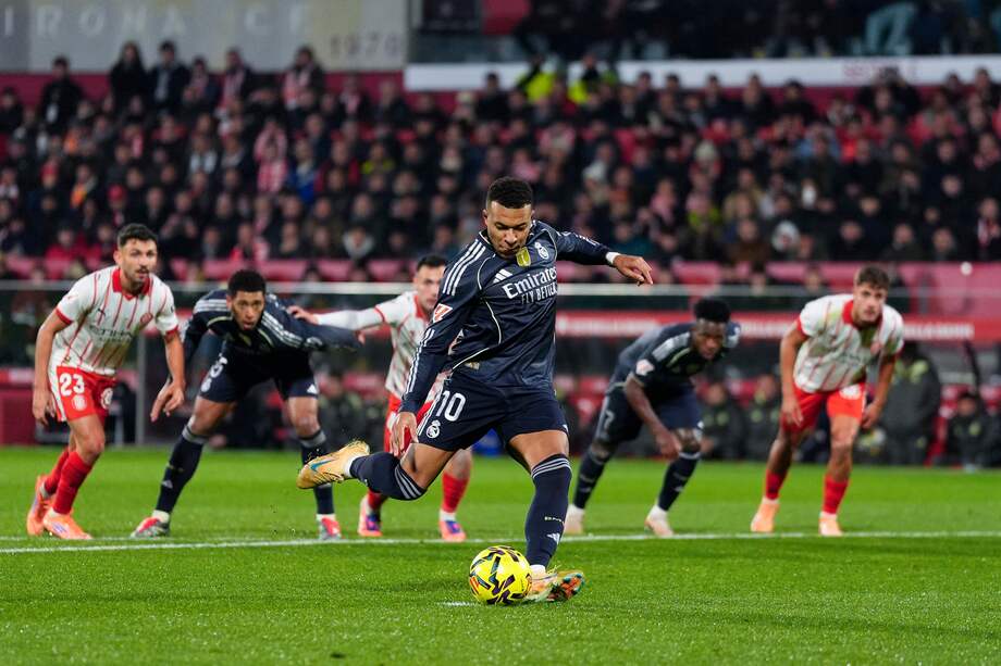 El delantero francés del Real Madrid, Kylian Mbappé, golpea el balón desde el punto de penalti para conseguir el primer gol del equipo madridista durante el encuentro correspondiente a la jornada 14 de Laliga EA Sports que disputan hoy domingo Girona y Real Madrid en el estadio Montilivi, en Girona.