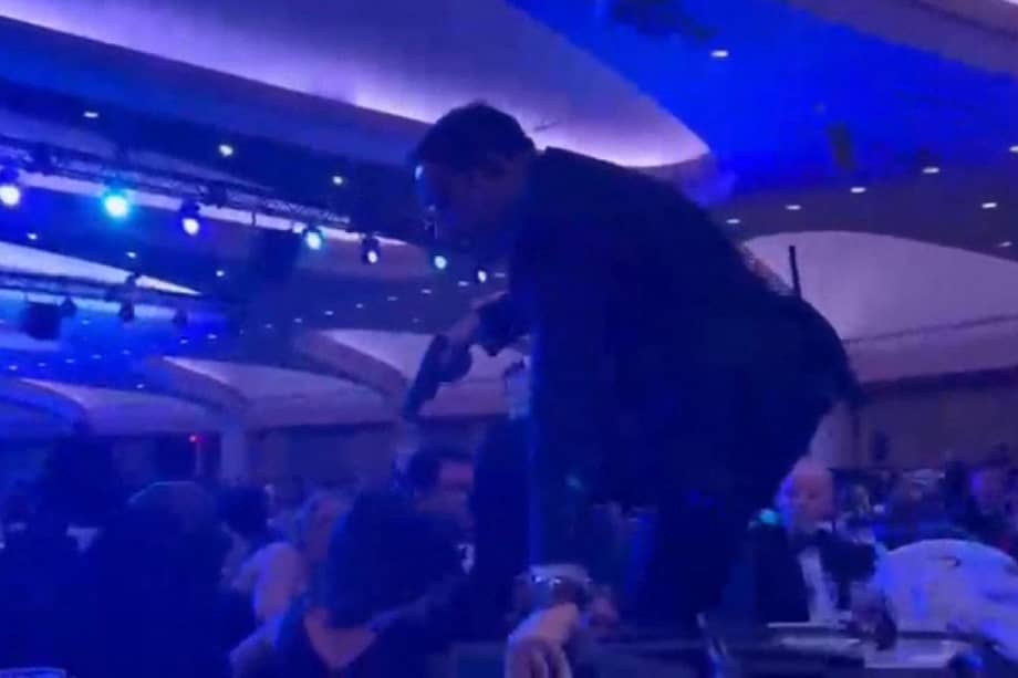 Esta captura de pantalla muestra a un agente armado que pasó por encima de las sillas para llegar al escenario donde estaba el presidente Donald Trump, tras escucharse fuertes disparos durante la cena de corresponsales de la Casa Blanca en el hotel Washington Hilton.