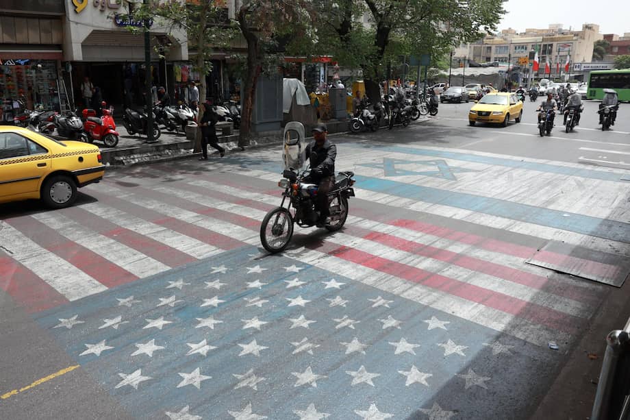 Un iraní pasa con su moto por encima de un cuadro que representa las banderas de Estados Unidos e Israel.