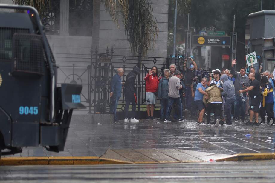 Personas se resguardan durante una manifestación el miércoles, frente al Congreso de la Nación en Buenos Aires (Argentina). Hinchas de más de 40 clubes de fútbol y las centrales obreras más grandes de Argentina acompañan a los jubilados en una movilización.