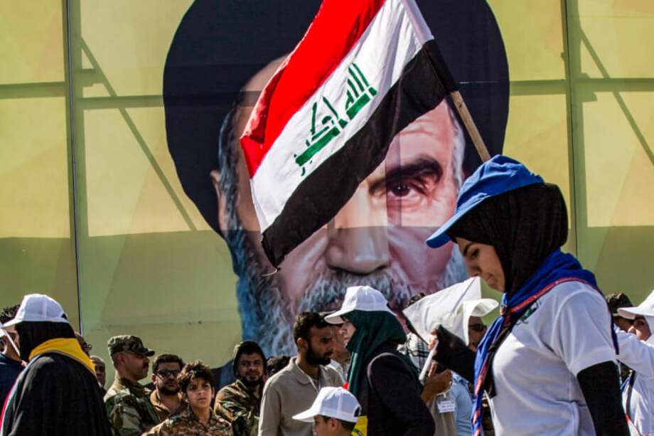 Una mujer iraquí marcha con otras personas ondeando una bandera nacional ante un retrato gigante que representa el rostro del fallecido líder iraní Ayatolá Ruholá Musawi Jomeini.
/ AFP