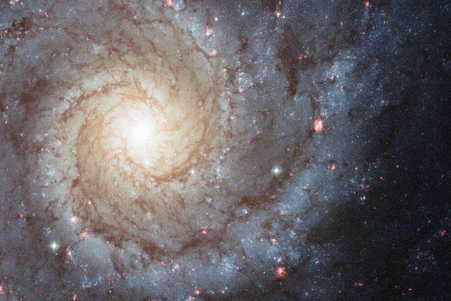 Messier 74 es ejemplo de una gran galaxia espiral que es vista por observadores de la Tierra casi de frente. Sus brazos espirales ricos emanan del núcleo central y están salpicados de cúmulos de estrellas azules jóvenes y regiones rosadas brillantes de hidrógeno ionizado (átomos de hidrógeno que han perdido sus electrones). / NASA