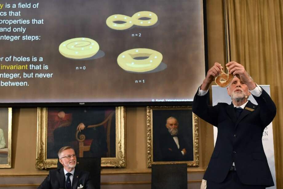 Thors Hans Hansson (derecha), miembro del Comité Nobel de Física, utiliza un pretzel para visualizar sus explicaciones durante una conferencia de prensa para anunciar los ganadores del Premio 2016 Nobel en Física. /AFP
