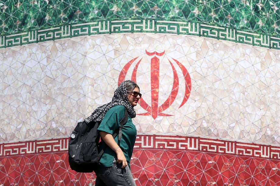 Una mujer iraní pasa junto a una valla publicitaria con la bandera nacional de Irán en la plaza Enqelab de Teherán, Irán, el 14 de junio de 2026.