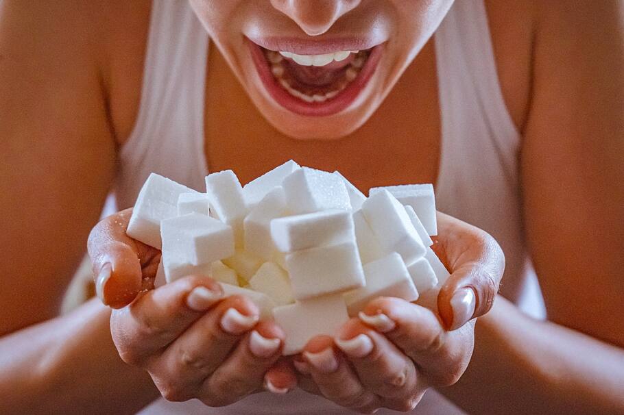 Close-up of woman holding a hands full of sugar cubes in front of her open mouth
