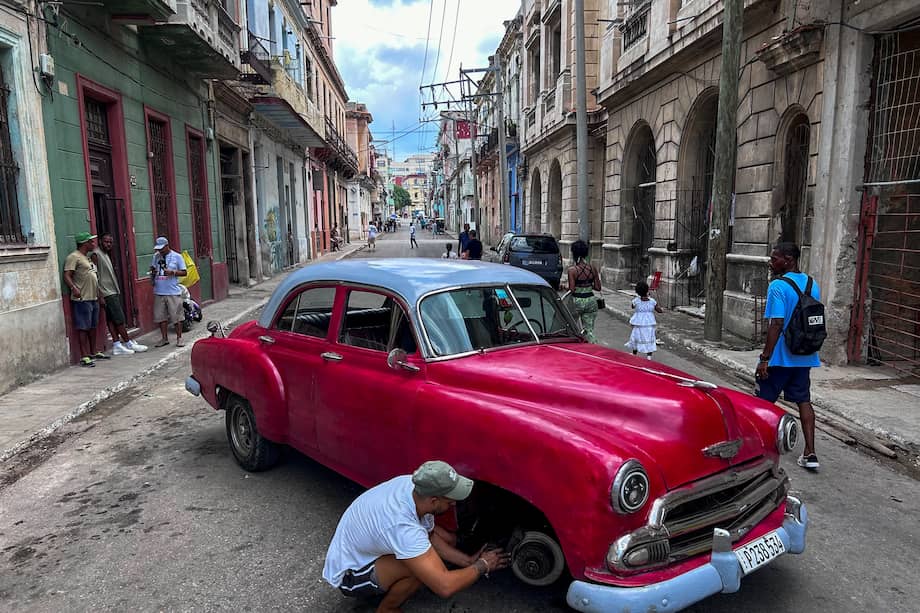 Un hombre repara un viejo carro americano en la mitad de una calle de La Habana.