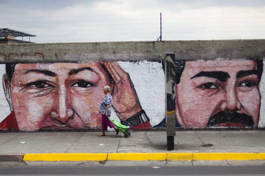 Una mujer camina frente a un muro con un graffiti del fallecido Hugo Chávez y el actual presidente venezonlano Nicolás Maduro. / AFP