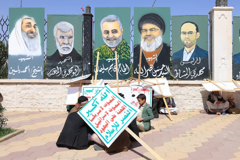 Partidarios de los hutíes se refugian del sol con carteles anti-EE.UU. e Israel debajo de pinturas de (der. a izq.) el alto funcionario hutí Mahdi al-Mashat, el difunto líder de Hezbolá Hassan Nasrallah, el general iraní Qasem Soleimani, el comandante de la milicia chií iraquí Abu Mahdi al-Muhandis y el líder de Hamás, el jeque Ahmed Yassin, durante una protesta contra Estados Unidos y contra Israel en Saná, Yemen, el 13 de junio de 2025.