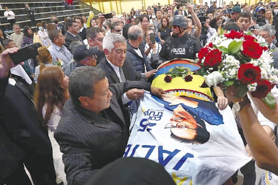 Varias personas colocan elementos como un cartel y un arreglo floral sobre el féretro del candidato Fernando Villavicencio, durante un velatorio público en un recinto ferial al que fue llevado previo a su entierro en Quito (Ecuador).