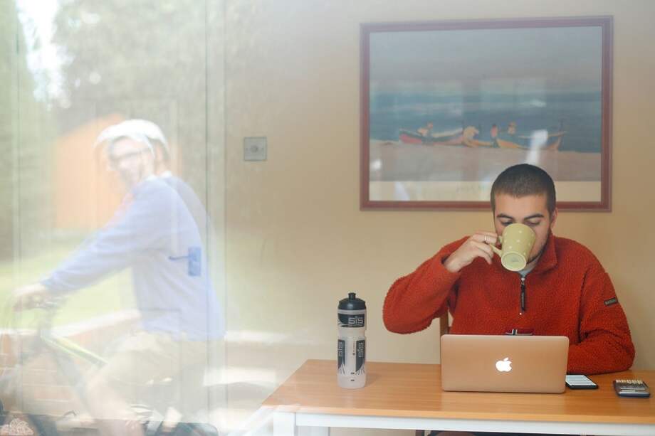 James Lewington estudia para su universidad mientras su padre Guy se refleja en la ventana de su casa en las afueras de Londres. La imagen hace parte de un ensayo fotográfico de AFP sobre la vida en confinamiento y la que se quedo fuera durante la pandemia.