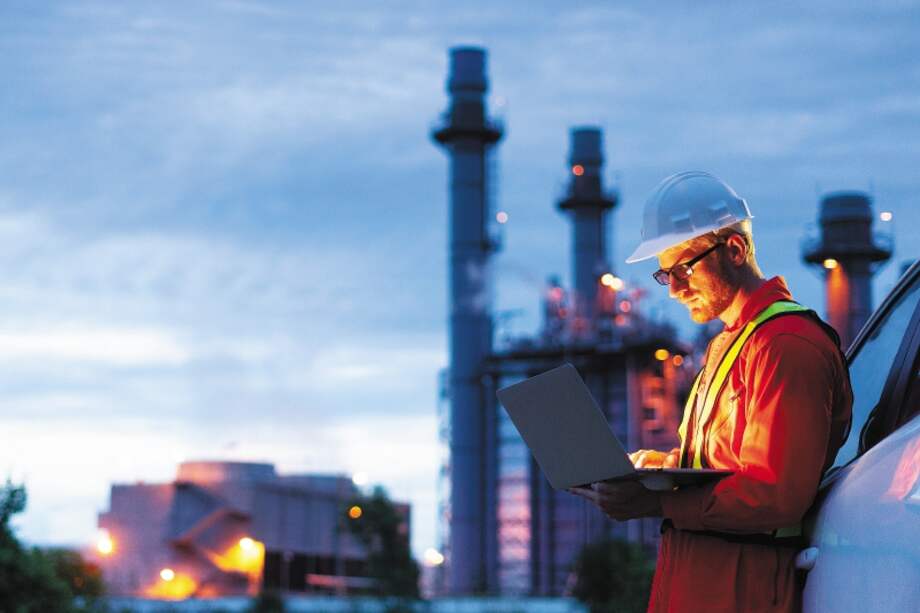 Engineer wearing safety helmet using Laptop with oil refinery background