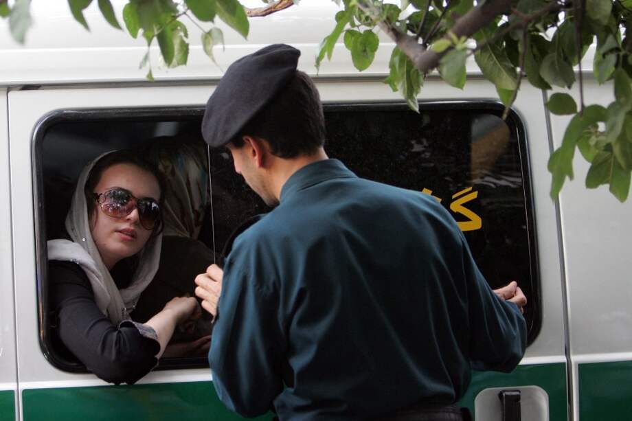 Un policía iraní habla con una mujer sentada en un coche de policía después de que fue arrestada por su ropa "inapropiada".