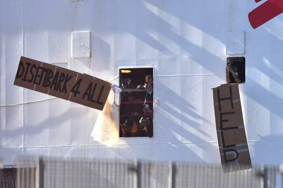Los migrantes rescatados muestran dos carteles en los que se lee "Ayuda" y "Desembarco para todos", mientras el barco está atracado en el muelle del puerto de Catania, Italia, este 8 de noviembre de 2022. Las autoridades italianas han permitido desembarcar en Reggio Calabria a un grupo de 89 solicitantes de asilo, pero más de 200 personas permanecen en otros dos barcos en Catania.