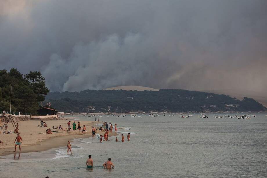 Personas nadando en la playa de Moulleau mientras el humo se eleva del incendio forestal en La Teste-de-Buch, en Francia.
