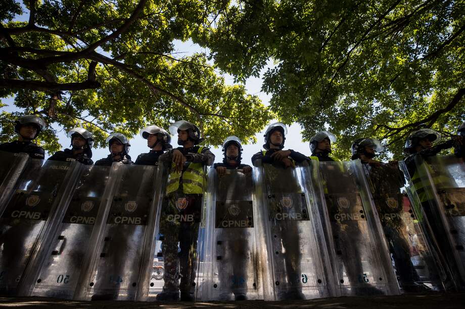 Policías vigilan a manifestantes que protestan por mejoras salariales en Caracas.