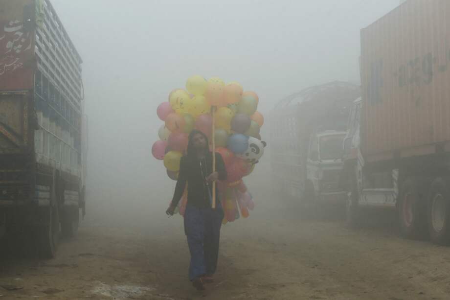 La foto, tomada el 9 de noviembre de 2017, muestra a un vendedor paquistaní cargando globos por la calle en medio del fuerte esmog en Lahore. / Arif Ali/AFP