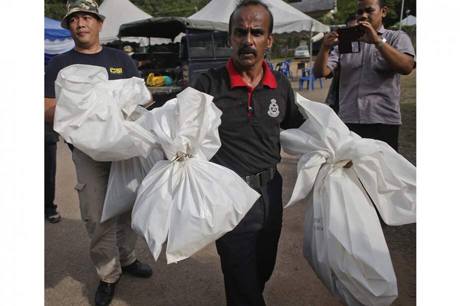 Un policía malasio se hace cargo de unas bolsas que contienen restos humanos en Wang Kelian (Malasia), lugar donde encontraron 28 campos clandestinos con fosas de inmigrantes./ EFE