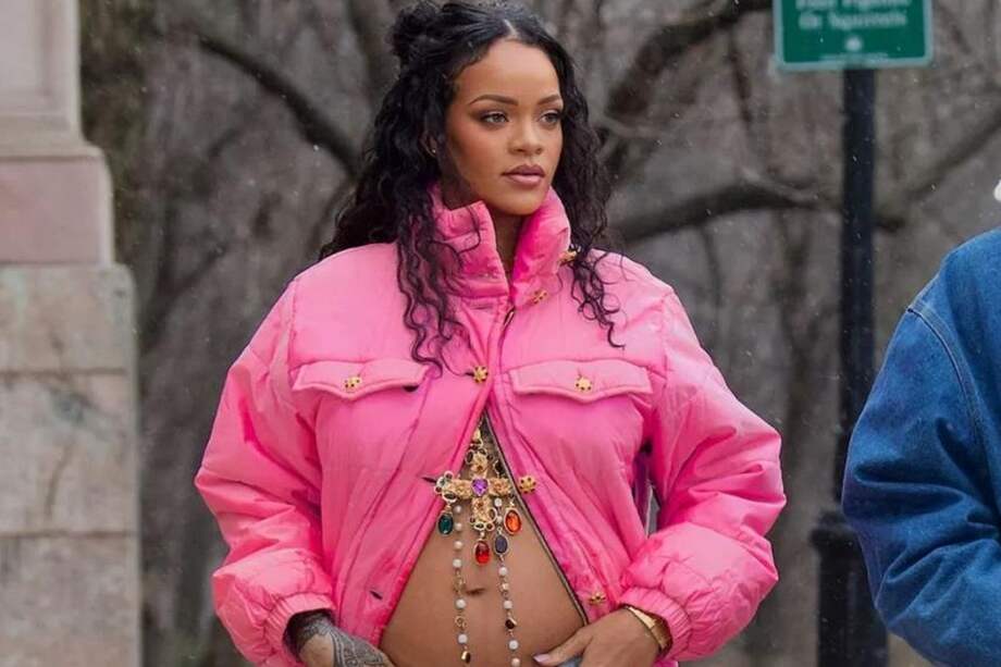 La artista se ve con un abrigo color rosa con una abertura que deja ver su barriga de varios meses de embarazo. Así mismo lleva un pantalón denim.