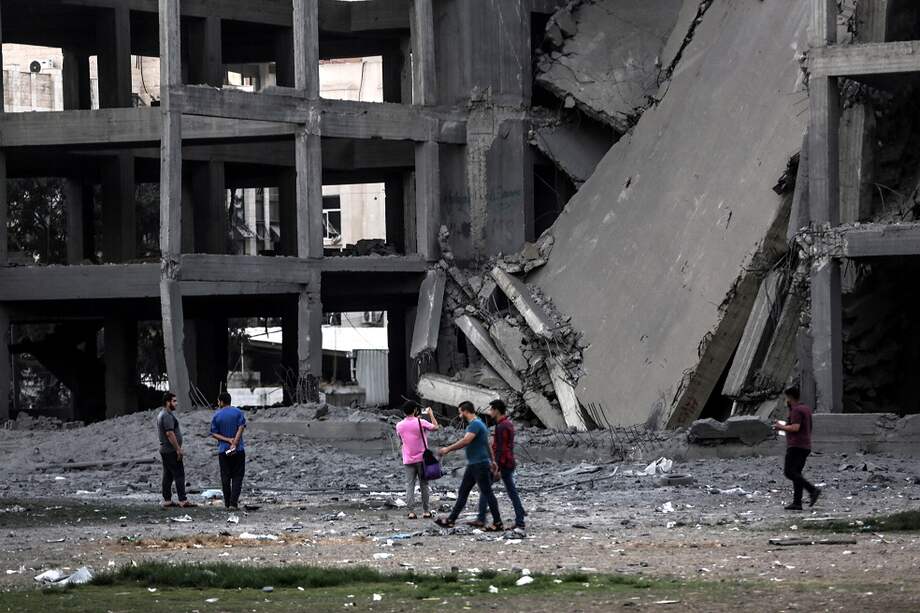 Palestinos caminando cerca a uno de los edificios bombardeados por Israel / EFE
